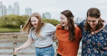 Drei junge Frauen am Wasser vor der Skyline einer Großstadt. - Copyright: Unsplash