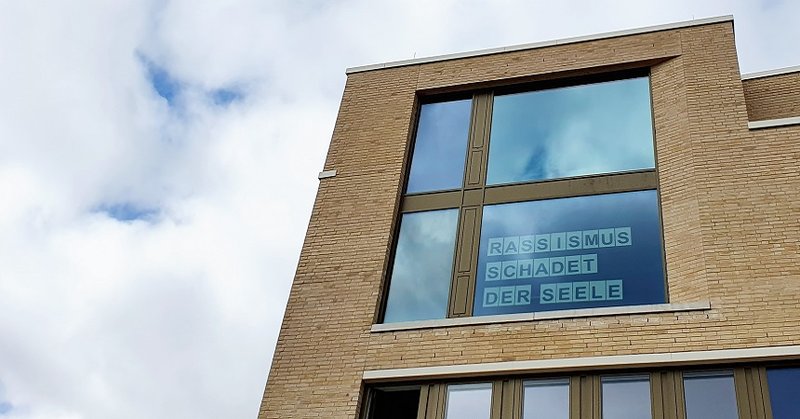 Haus der Kirche großes Fenster, Schriftzug Rassismus